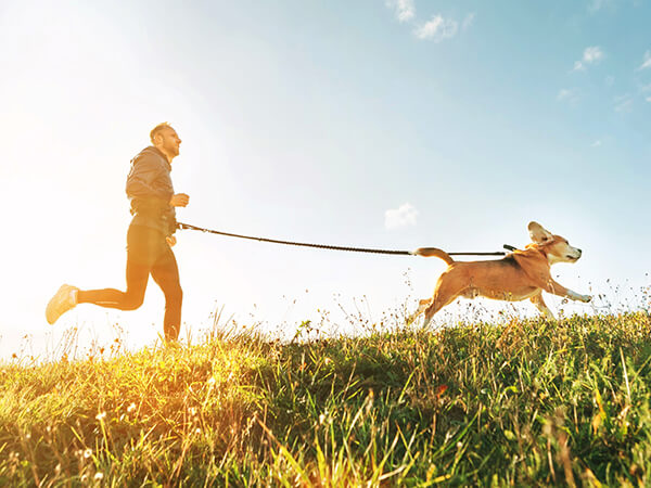 man running through field with dog on leash